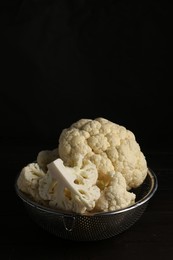 Photo of Colander with fresh raw cauliflower on black wooden table