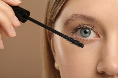 Photo of Woman applying mascara onto eyelashes against light brown background, closeup