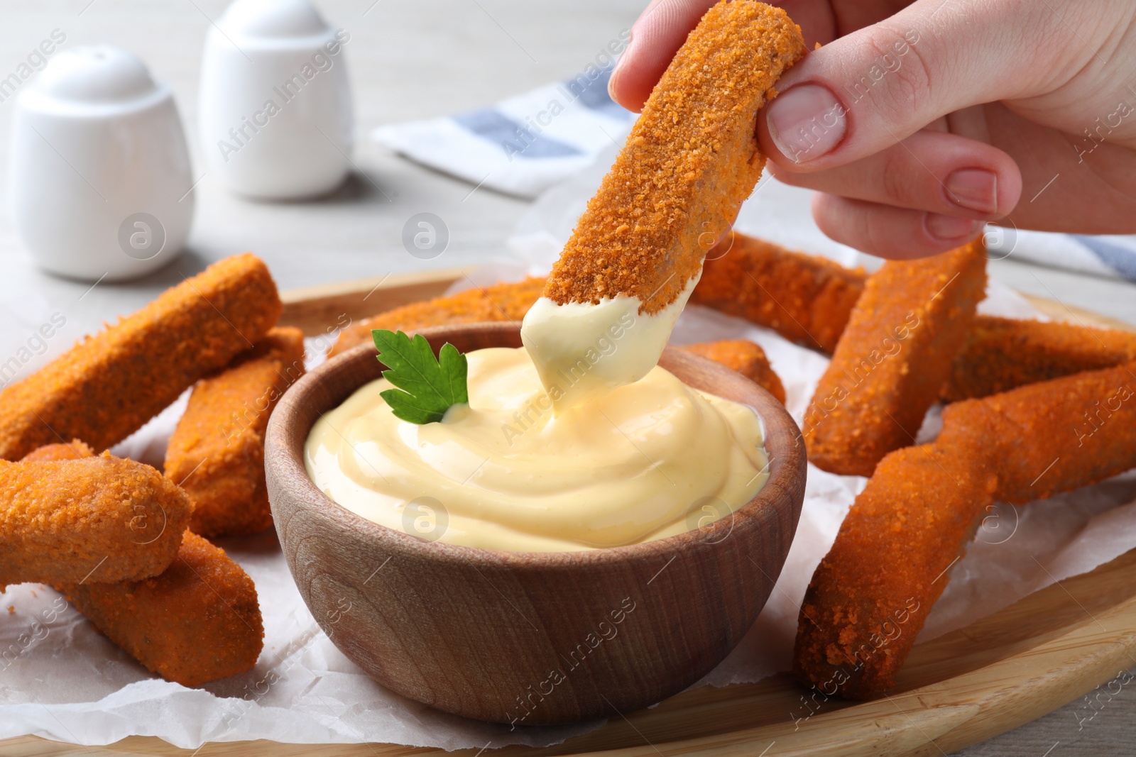 Photo of Woman dipping delicious chicken nuggets into cheese sauce at table, closeup