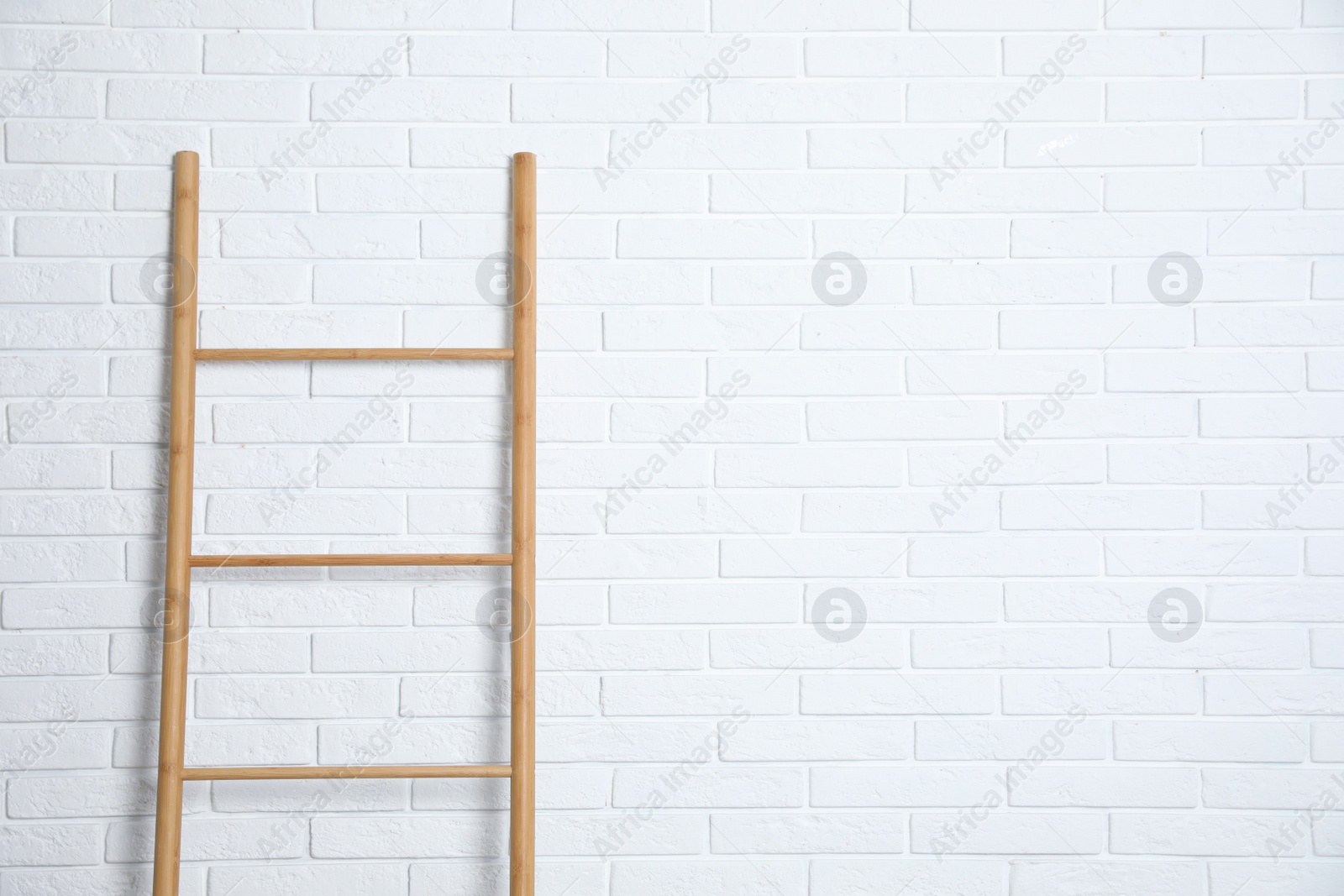 Photo of Modern wooden ladder near white brick wall. Space for text