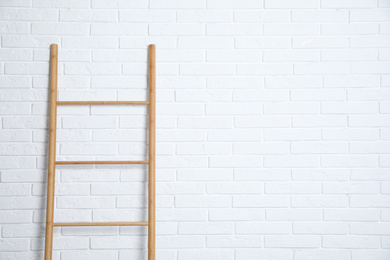 Photo of Modern wooden ladder near white brick wall. Space for text