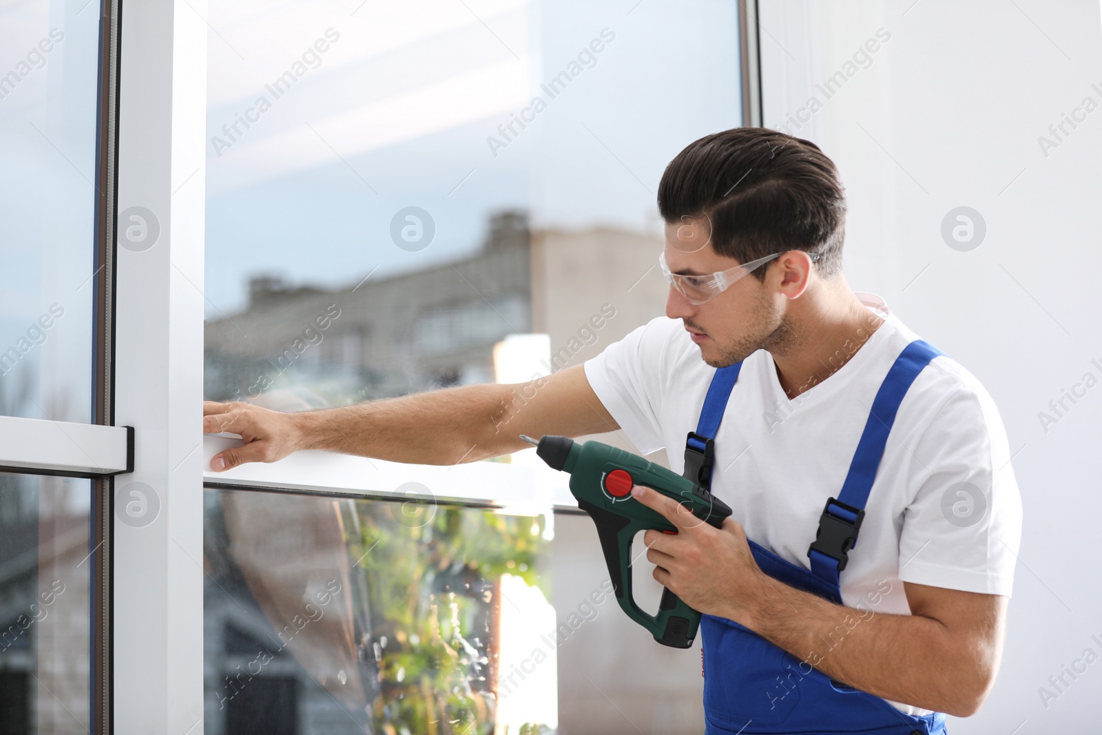 Photo of Construction worker repairing plastic window with electric screwdriver indoors