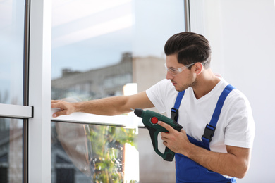 Construction worker repairing plastic window with electric screwdriver indoors