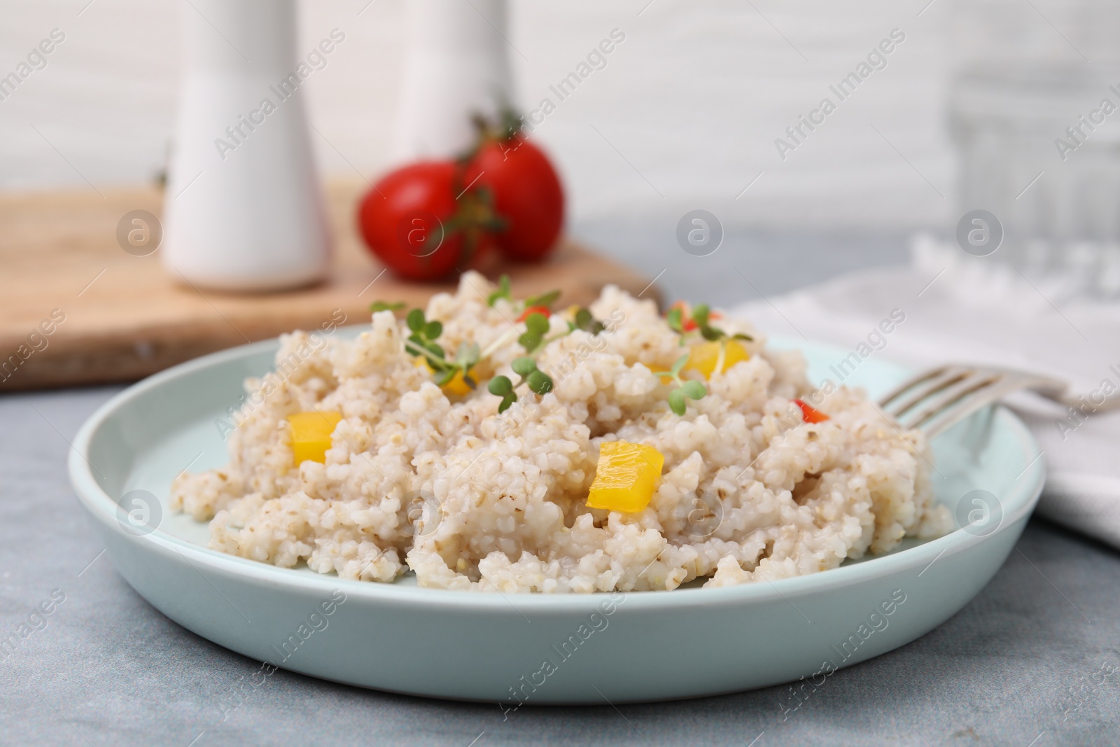 Photo of Delicious barley porridge with vegetables and microgreens on gray table, closeup