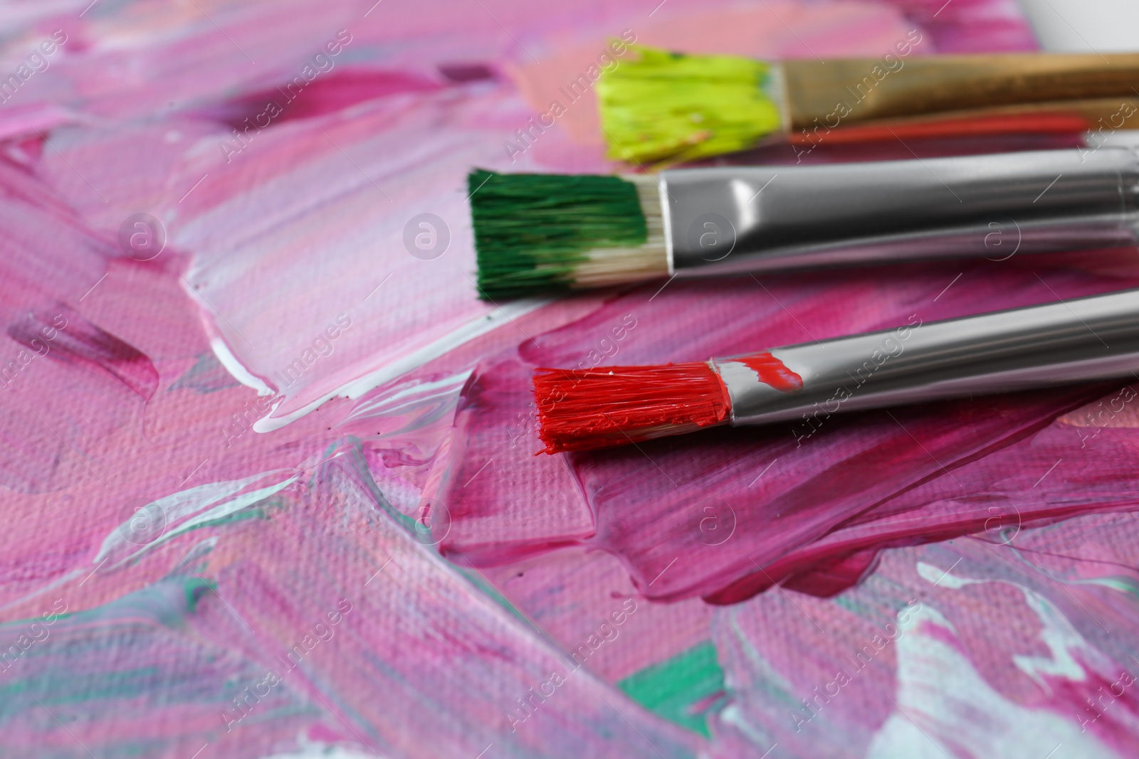 Photo of Set of different brushes on abstract colorful paint, closeup