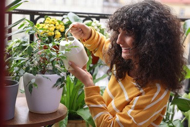 Beautiful young woman watering green houseplants on balcony