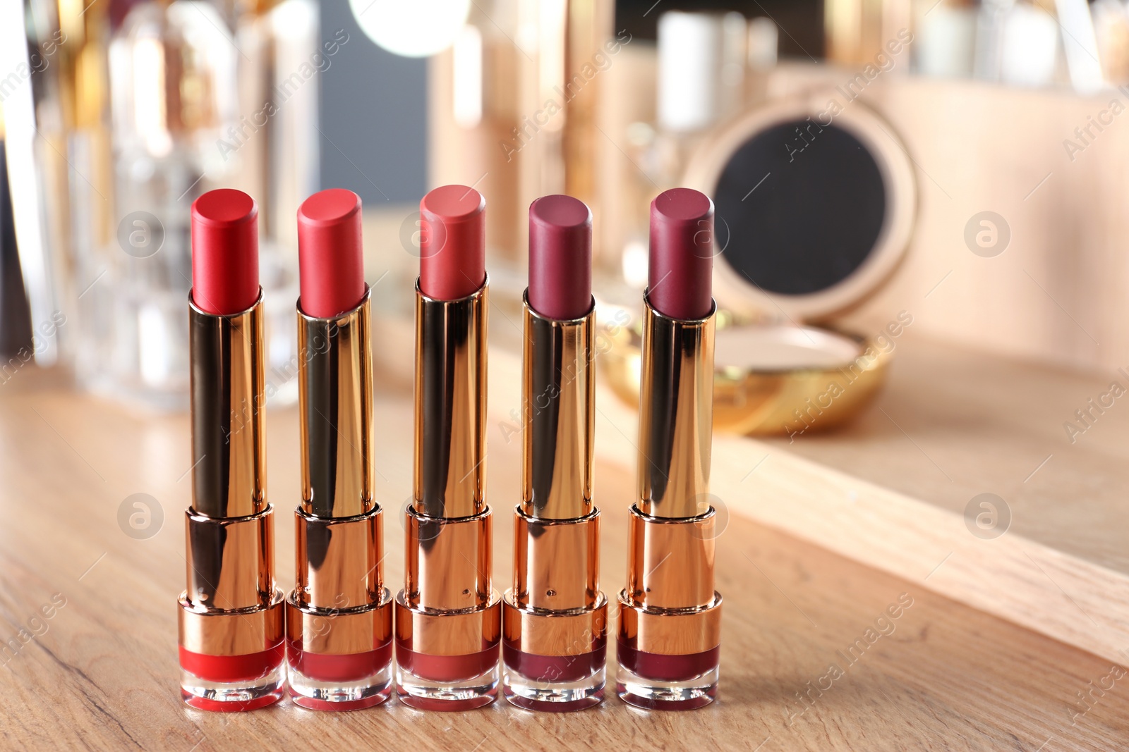 Photo of Set of bright lipsticks in gold tubes on dressing table