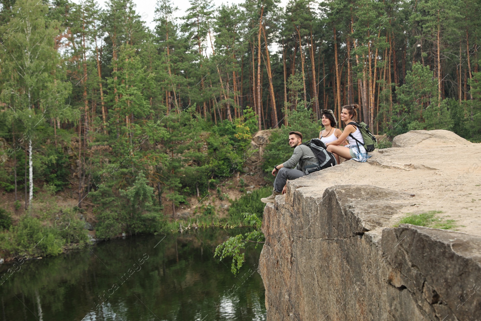 Photo of Young friends on rocky mountain near lake. Camping season