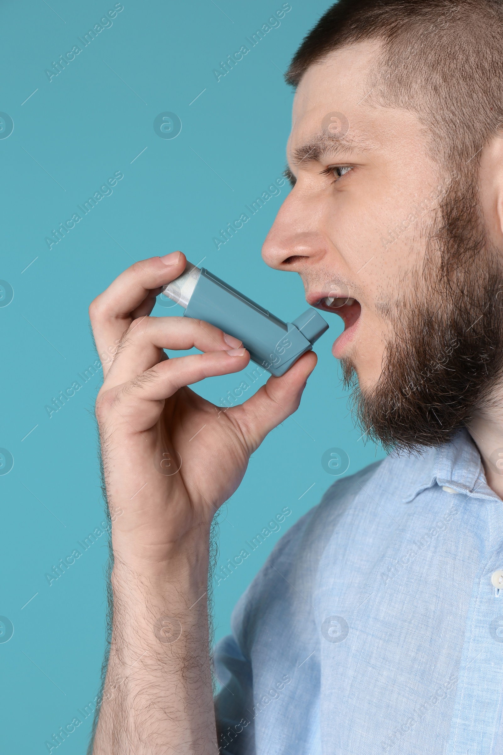 Photo of Young man using asthma inhaler on color background