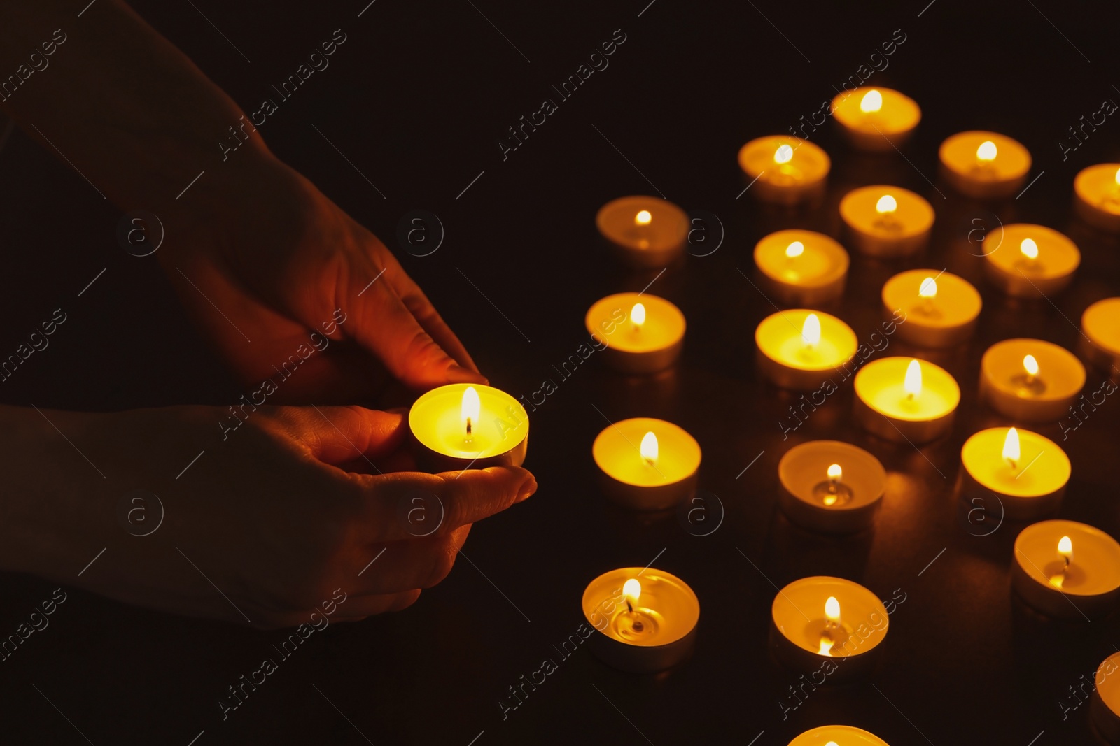 Photo of Young person holding burning candle in darkness, closeup