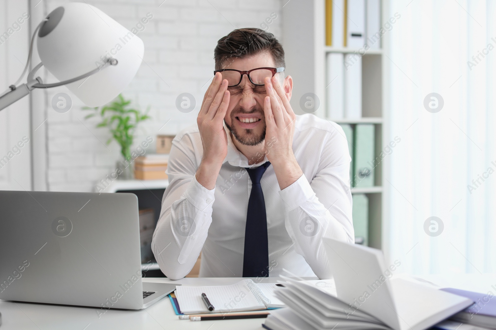 Photo of Man suffering from headache while sitting at table in office