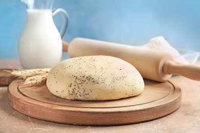 Photo of Raw dough with poppy seeds and rolling pin on wooden board