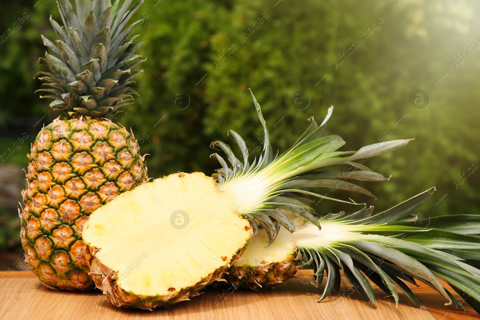 Photo of Delicious ripe pineapples on wooden table outdoors, space for text