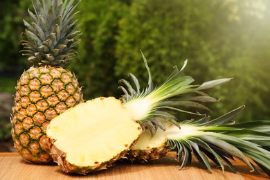 Delicious ripe pineapples on wooden table outdoors, space for text