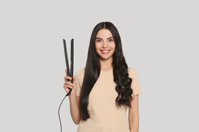 Photo of Beautiful happy woman with hair iron on light grey background