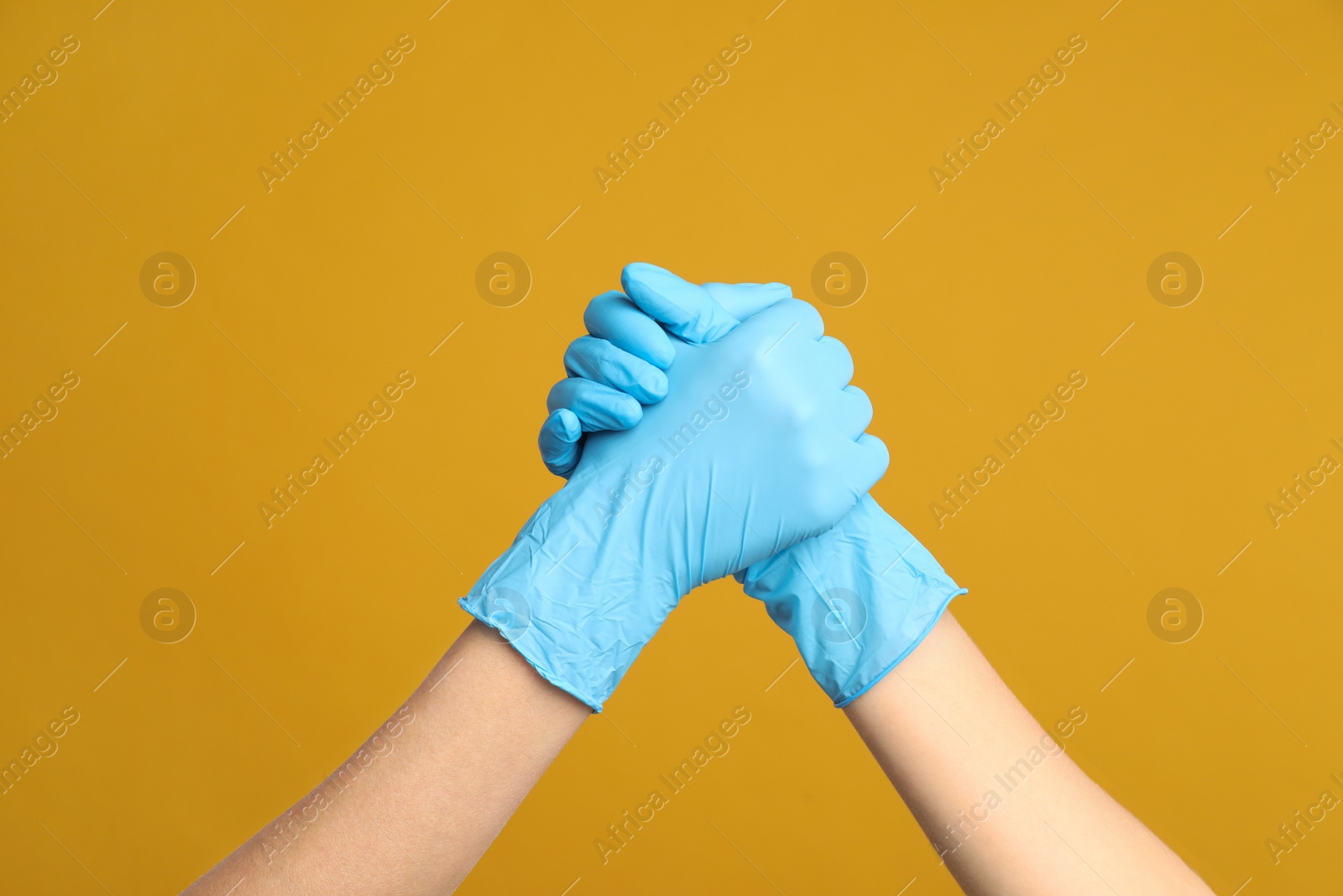 Photo of Doctors in medical gloves shaking hands on yellow background, closeup