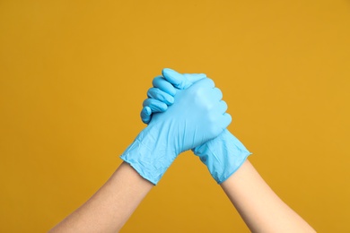 Doctors in medical gloves shaking hands on yellow background, closeup