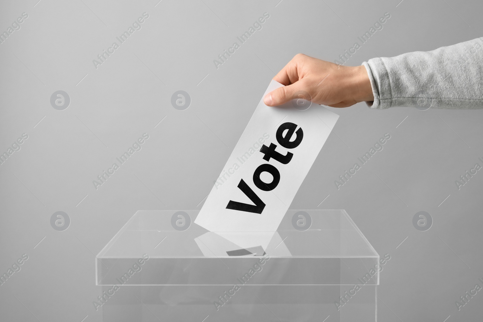 Photo of Man putting his vote into ballot box on light background, closeup