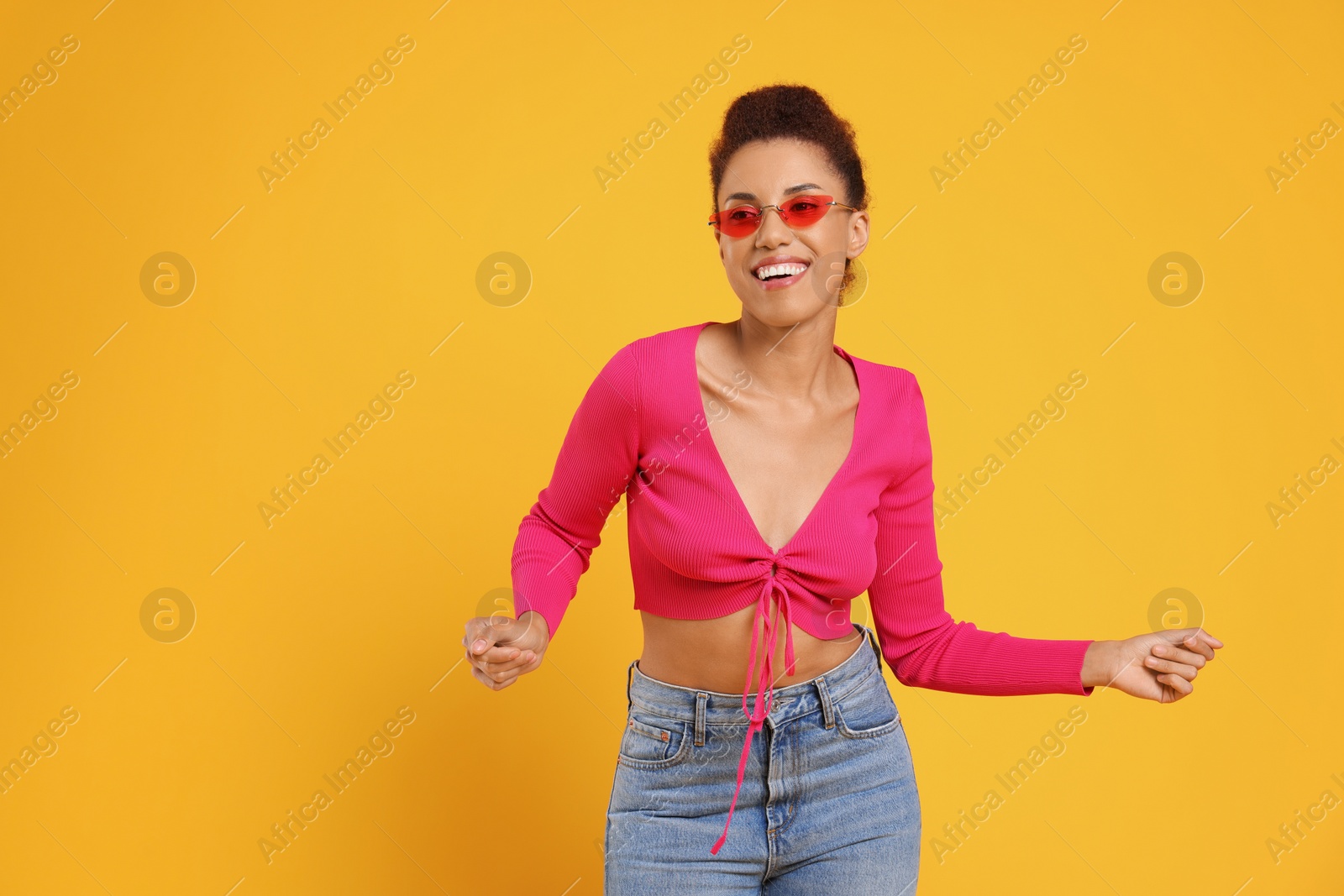 Photo of Happy young woman in stylish sunglasses dancing on orange background. Space for text