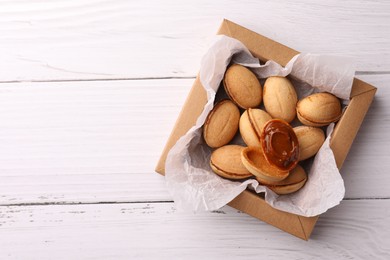 Photo of Delicious nut shaped cookies with boiled condensed milk in box on white wooden table, top view