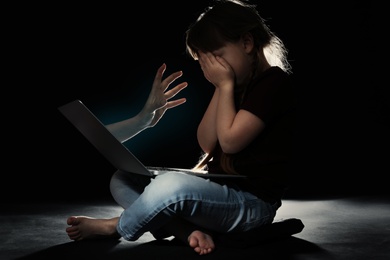 Stranger reaching frightened little child with laptop on dark background. Cyber danger