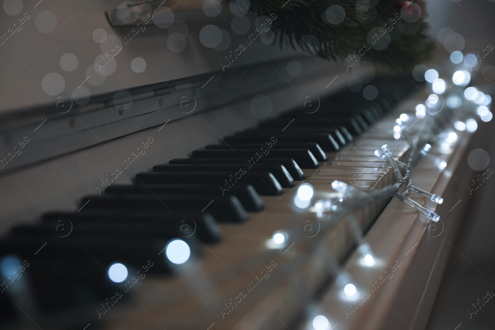 Photo of Glowing fairy lights on piano keys indoors, closeup. Christmas music