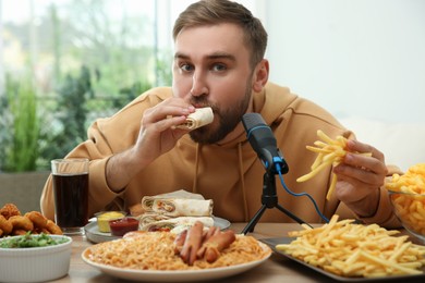 Food blogger eating near microphone at table in room. Mukbang vlog