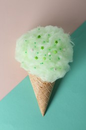 Sweet cotton candy in waffle cone on color background, top view