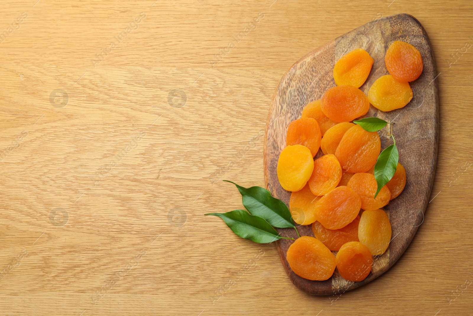 Photo of Tasty apricots and green leaves on wooden table, top view with space for text. Dried fruits