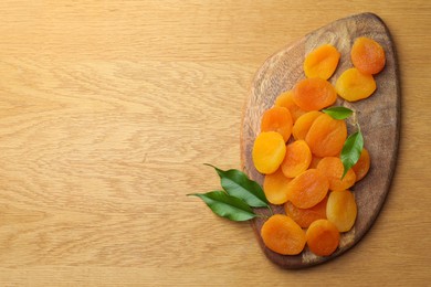 Photo of Tasty apricots and green leaves on wooden table, top view with space for text. Dried fruits