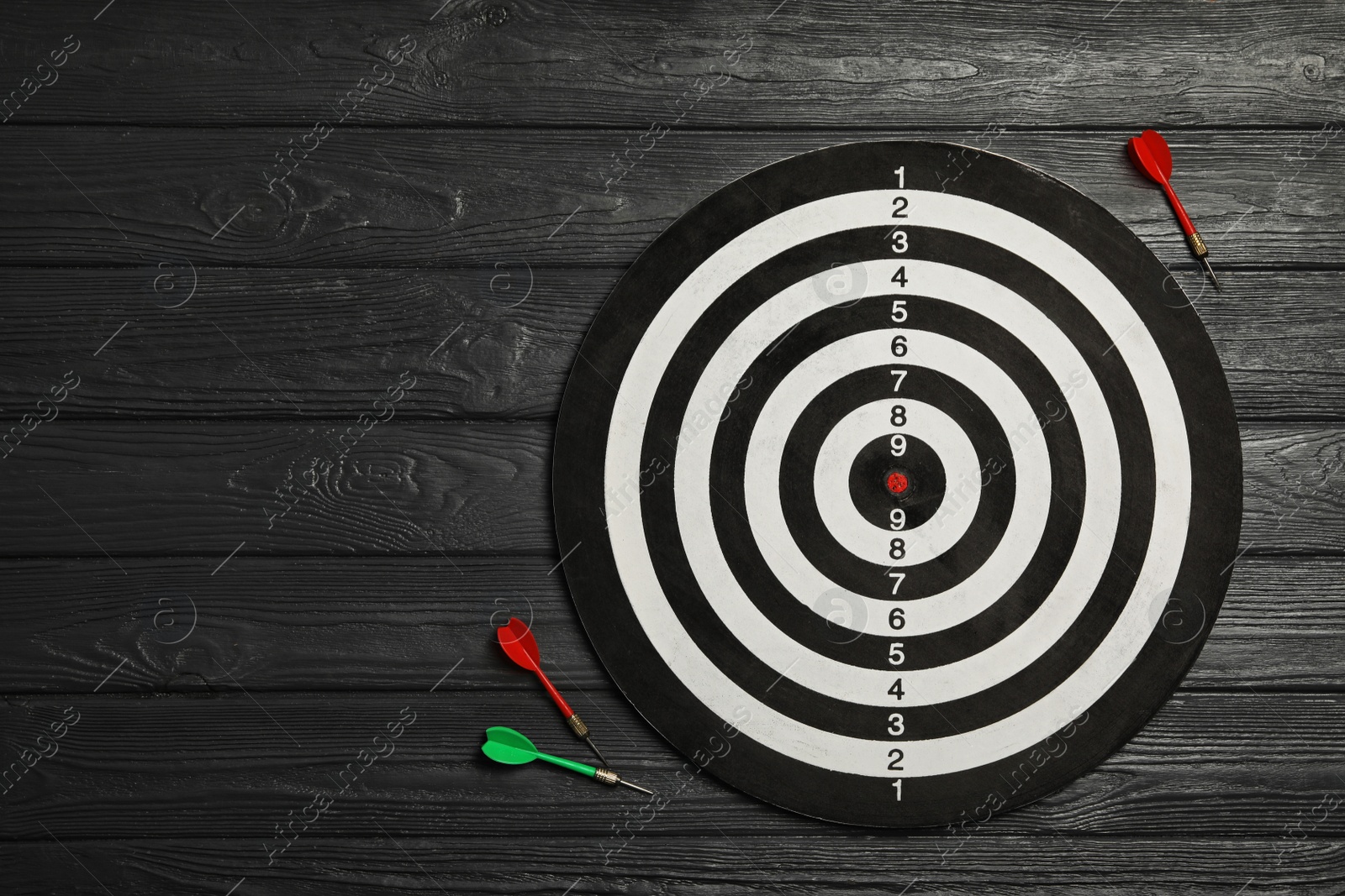 Photo of Dart board with color arrows on black wooden background, top view. Space for text