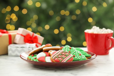 Photo of Decorated cookies and hot drink on white marble table against blurred Christmas lights