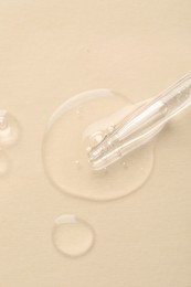 Glass pipette and transparent liquid on beige background, top view