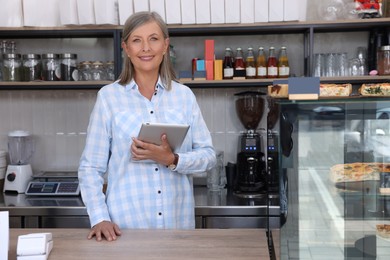 Photo of Happy business owner with tablet at cashier desk in her cafe