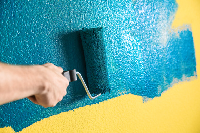 Photo of Man painting yellow wall with blue dye, closeup