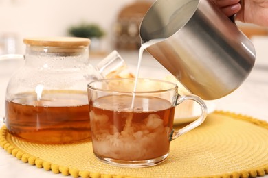 Photo of Woman pouring milk in tea at table, closeup