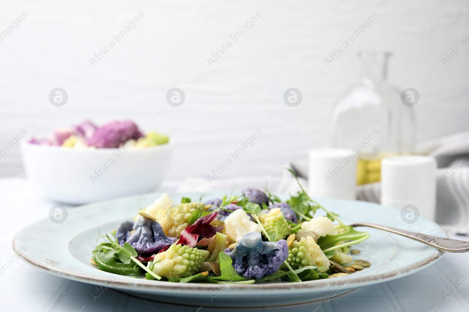 Photo of Delicious salad with cauliflower and pumpkin seeds served on white tiled table, closeup
