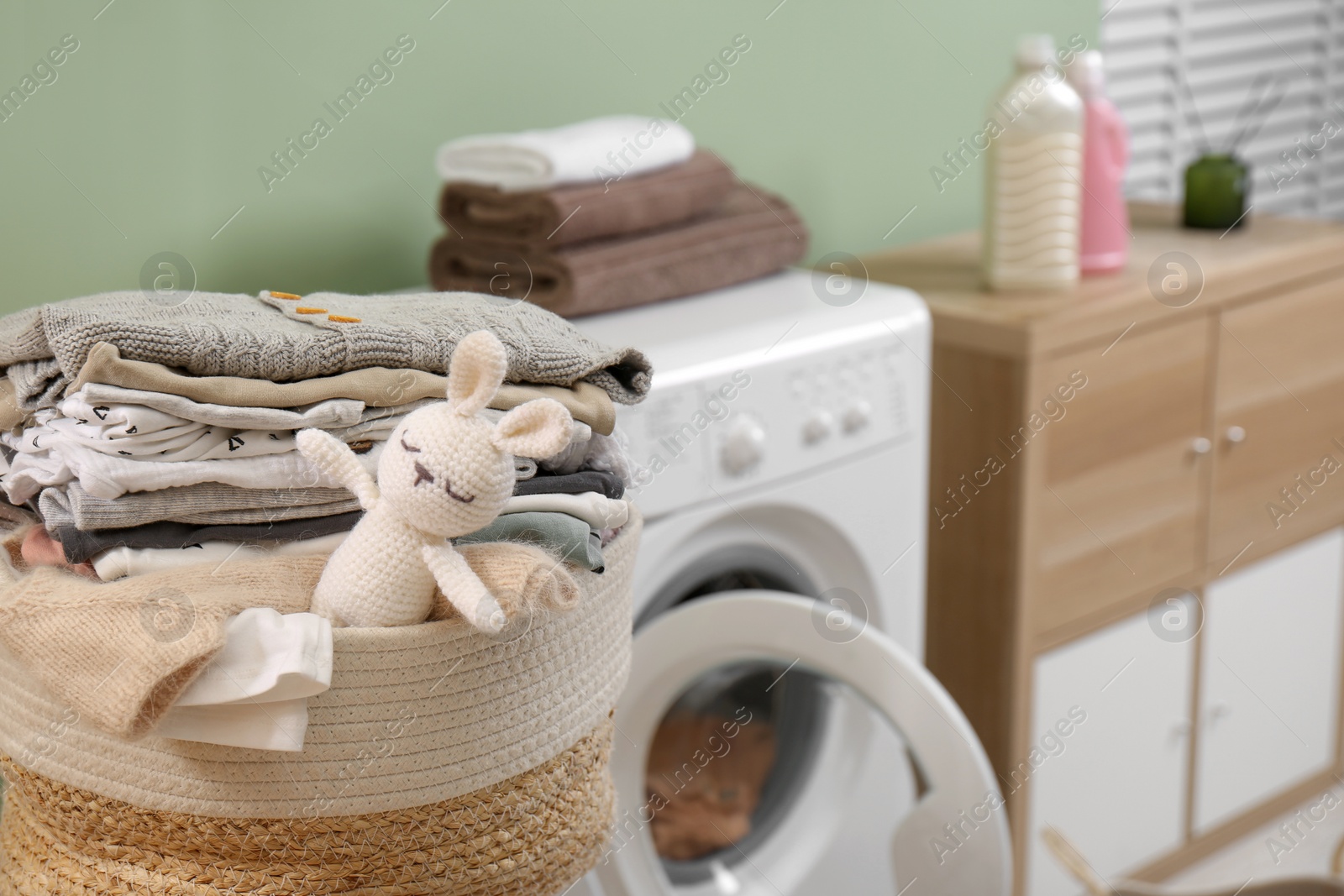 Photo of Laundry basket with baby clothes and toy in bathroom, closeup. Space for text