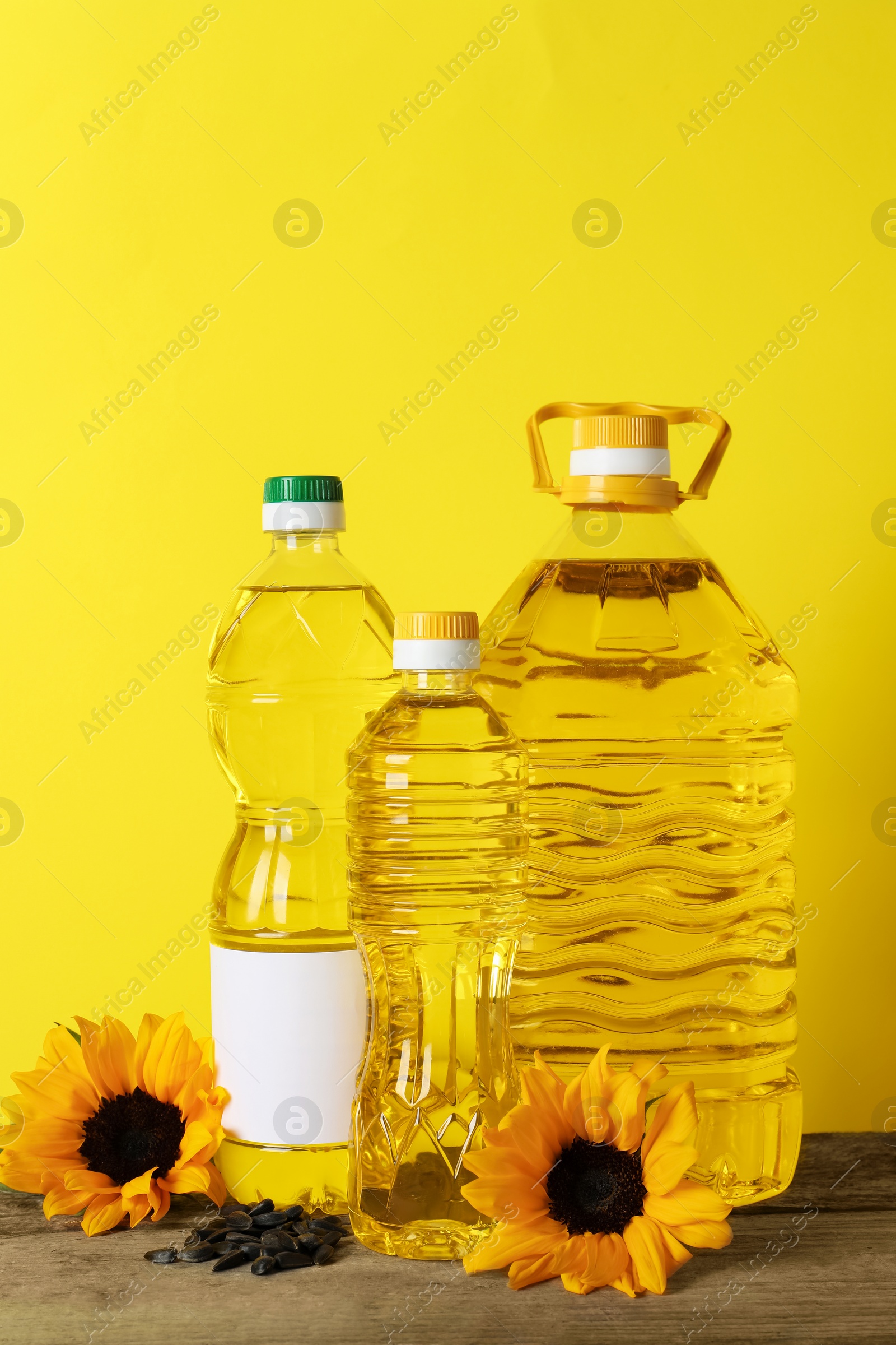 Photo of Bottles of cooking oil, sunflowers and seeds on wooden table