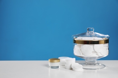 Jar with cotton pads on white table against blue background. Space for text