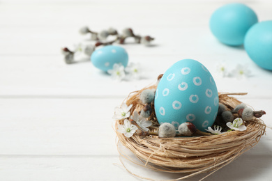 Colorful Easter egg in decorative nest on white wooden table. Space for text