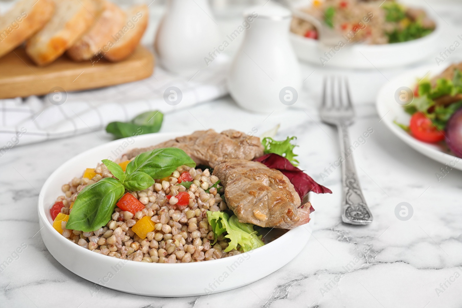 Photo of Tasty buckwheat porridge with meat on white marble table