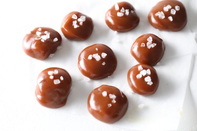 Photo of Tasty caramel candies and salt on white table, closeup