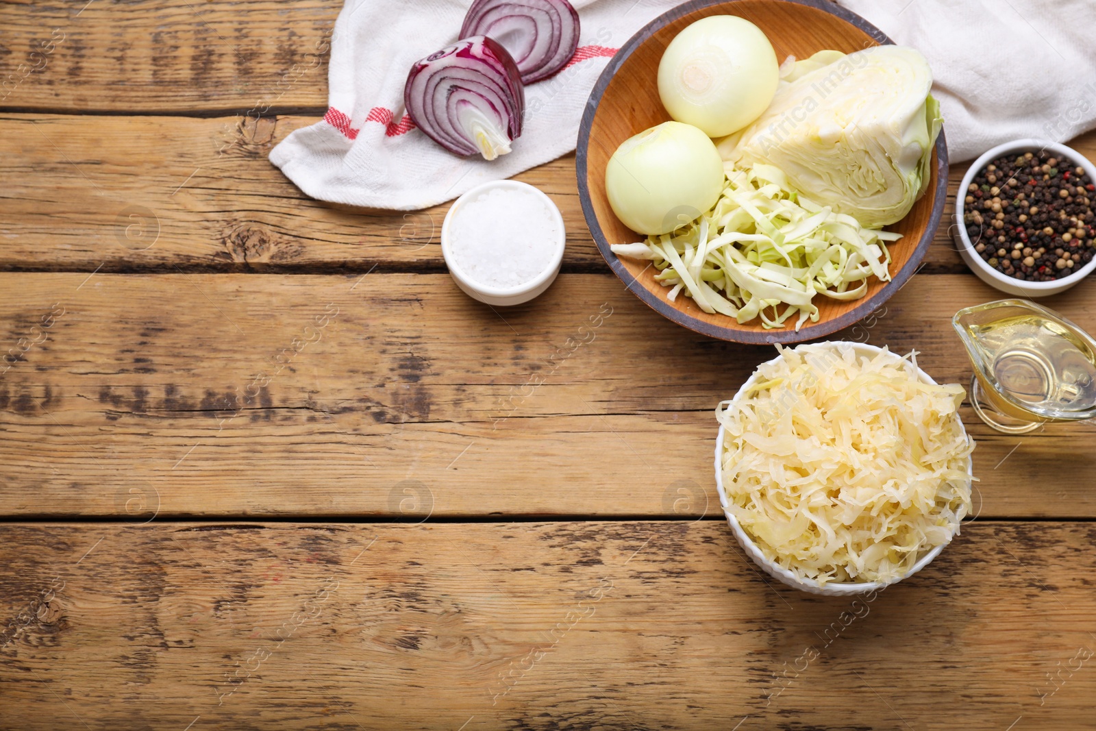 Photo of Bowl of tasty sauerkraut and ingredients on wooden table, flat lay. Space for text