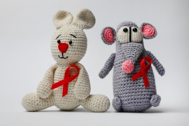 Photo of Cute knitted toys with red ribbons on light grey background. AIDS disease awareness