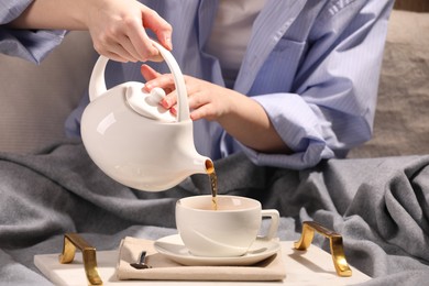 Woman pouring aromatic tea into cup at table, closeup