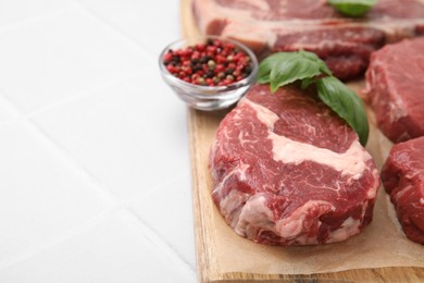 Photo of Cut fresh beef meat, spices and basil leaves on white tiled table, closeup. Space for text