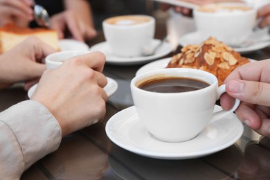 Photo of Friends drinking coffee at wooden table in outdoor cafe, closeup