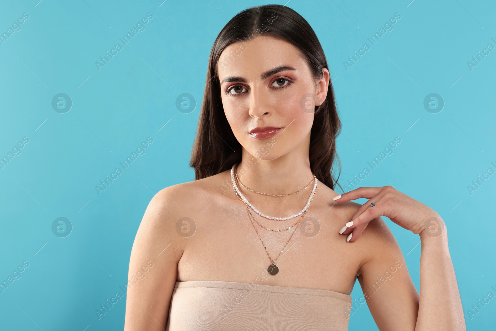 Photo of Beautiful woman with elegant necklaces on light blue background