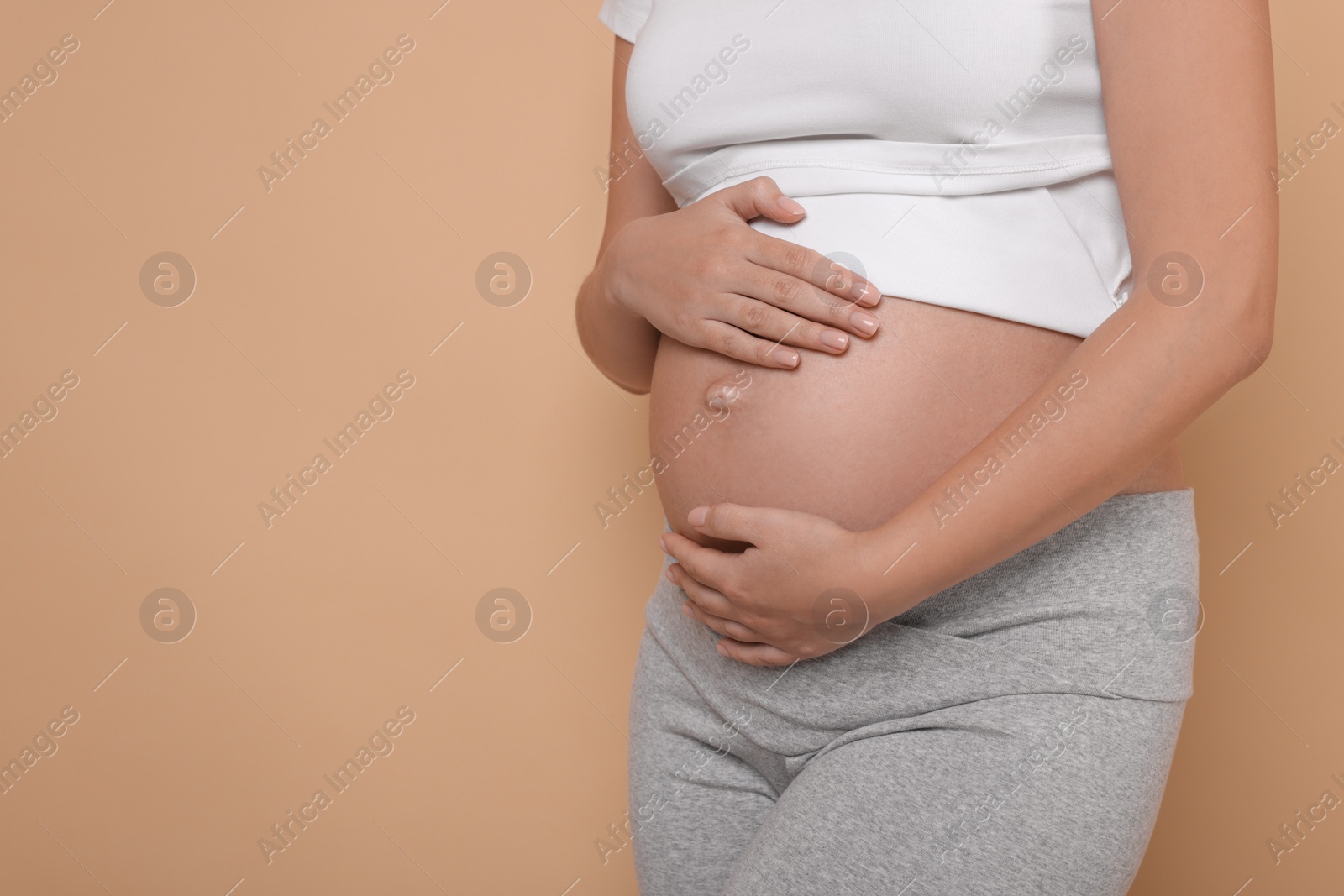 Photo of Pregnant woman in white T-shirt on beige background, closeup. Space for text